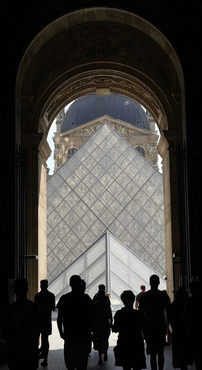 Un groupe franchit le passage voûté qui ouvre sur la pyramide du Louvre.